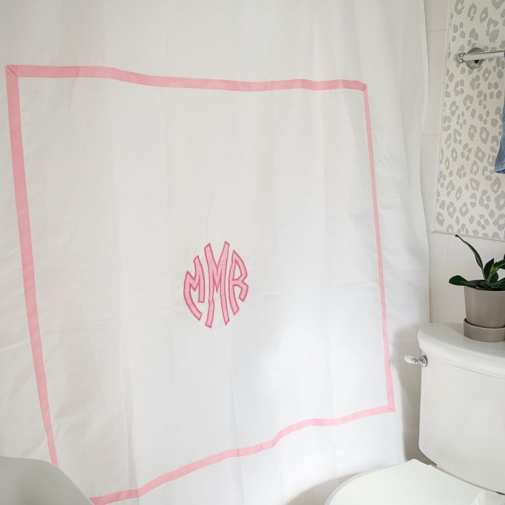 a monogrammed shower curtain in a bathroom with pink trim on the border and white toilet