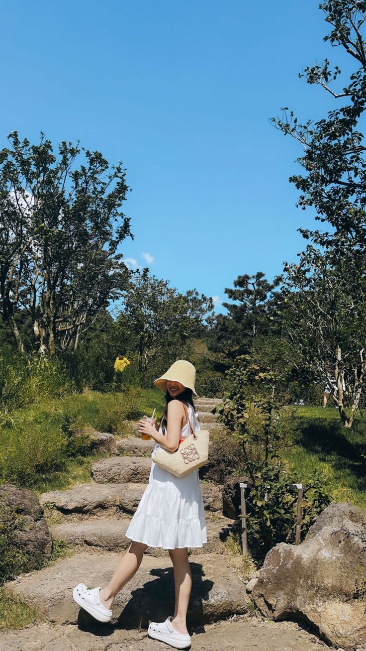 a woman in a white dress and hat walking down a path