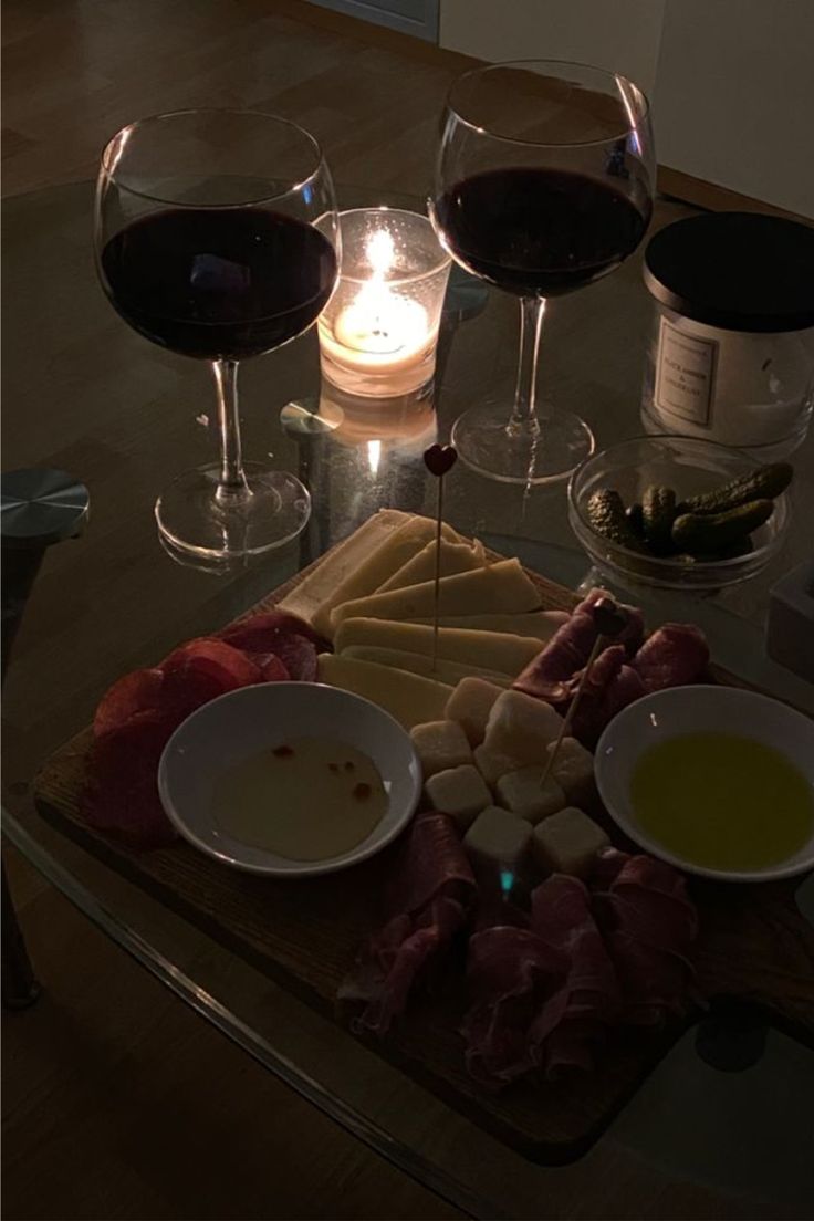 two glasses of wine are sitting on a table with cheese, meats and crackers