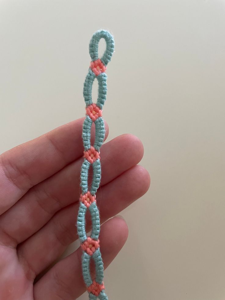 a hand holding a small blue and pink beaded bracelet with an o - ring