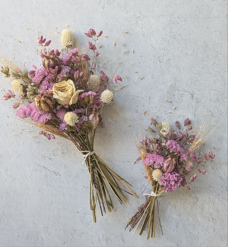 two bouquets of dried flowers sitting on top of a white wall next to each other