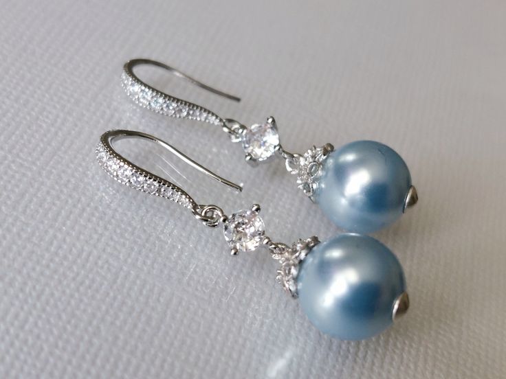 two pairs of blue and white pearls are hanging from silver earwires on a white cloth