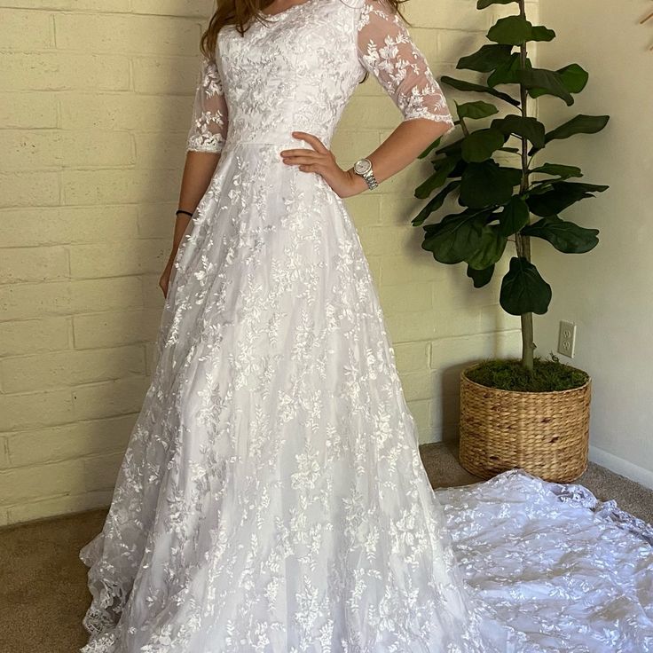 a woman in a white wedding dress standing next to a plant