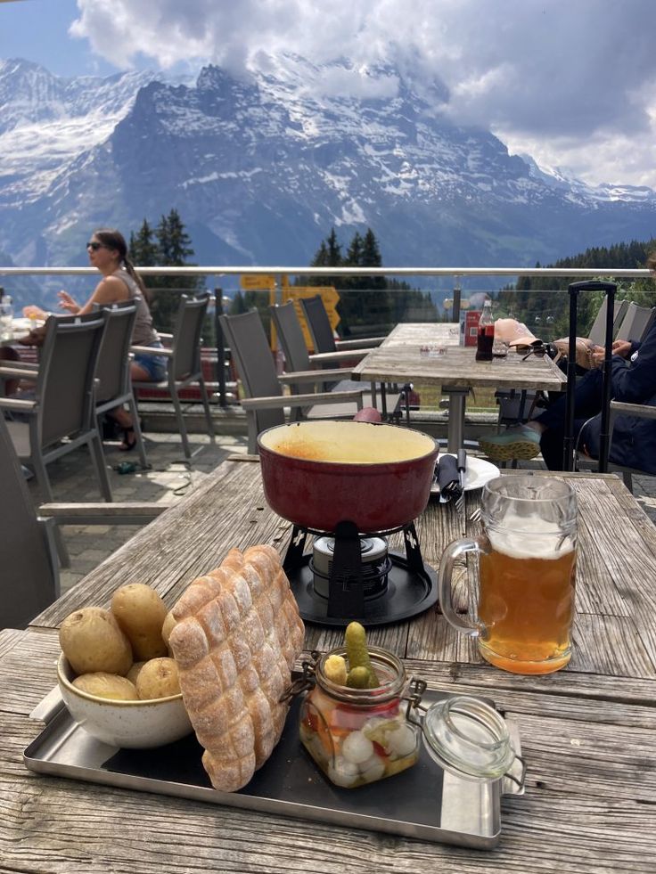 a table topped with food and drinks on top of a wooden deck next to mountains