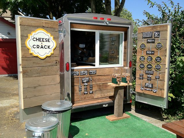 the food truck is made out of wood and has cheese cracker signs on it