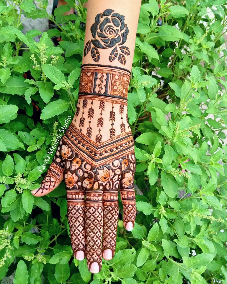 a henna tattoo on someone's hand in front of green leaves and bushes