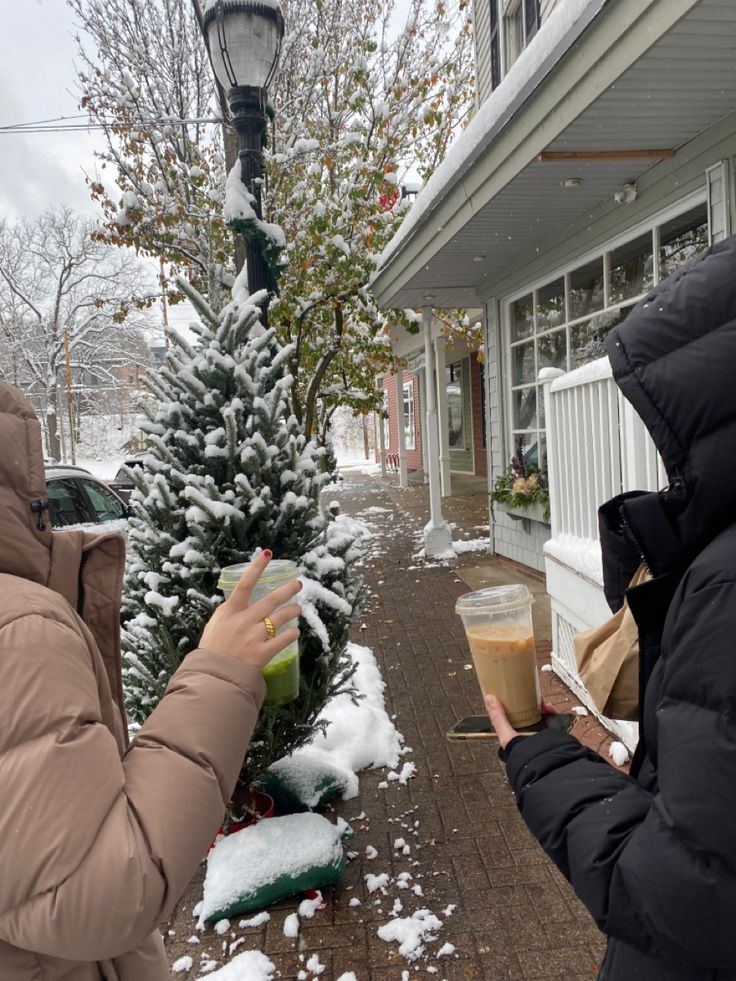 two people standing in front of a house with snow on the ground and one person holding a drink