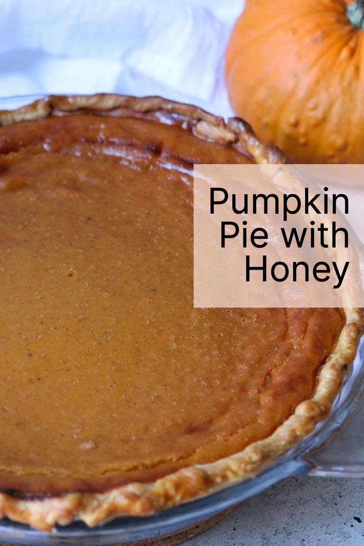 pumpkin pie with honey crust in glass pie dish on white tablecloth next to orange pumpkins