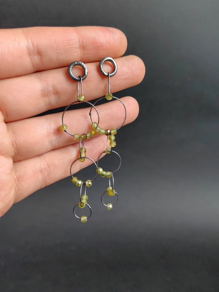 This listing is for a super delicate pair of earrings. Hanging from a handmade sterling silver stud, the light hammered links and  these beautiful faceted pieces olive green Cubic Zirconia, the cut makes them shine so much, and they have a light change in hues! Each of the links has been formed by hand and then hammered, this light hammering hardens and makes the links keep their shape, the beads are free to move around making for a very attractive pair of earrings :) They are 7.2cms long. Made using sterling silver, darkened then polished for a shiny dark finish that makes the beads really pop. Matching chain and other earrings with different beads  available: https://www.etsy.com/shop/Nataliaraya Thank you for taking the time to read this! ------------------------------------------------ Kinetic Earrings, Earrings Hanging, Artisan Jewelry Handmade, Oxidized Silver, Sterling Silver Studs, Handmade Sterling Silver, Handmade Artisan, Stone Jewelry, Beaded Earrings