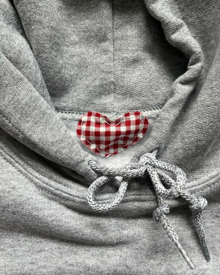 a red and white checkered heart on the back of a gray hoodie with a pair of scissors sticking out of it