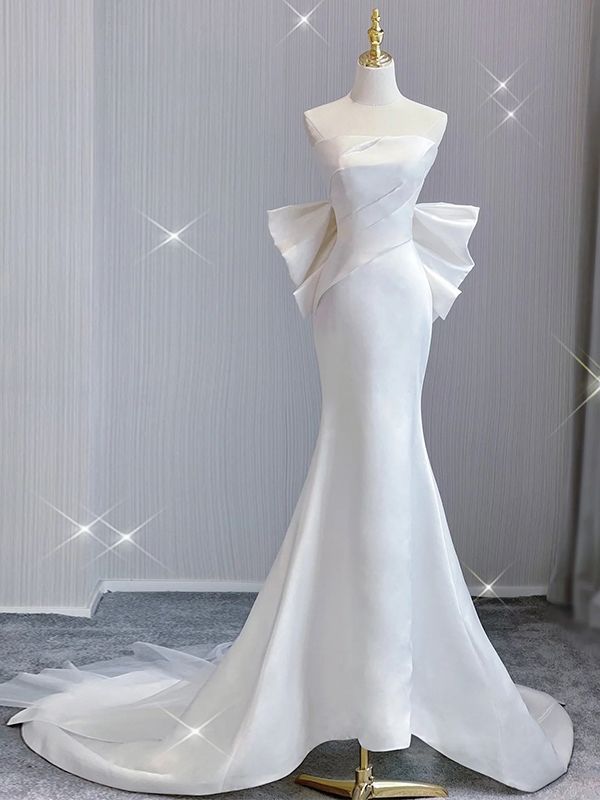 A row of fabric-covered buttons runs from the center back to the hem, adding a sophisticated touch to the design. The back is completed with a discreet zipper-up closure for a secure and seamless fit. A built-in bra provides additional support and confidence as you walk down the aisle. Strapless Wedding Dress With Bow, Satin Fitted Wedding Dress, Satin Strapless Wedding Dress, Wedding Dresses With Bow, Wedding Dress With Bow, Satin Mermaid Wedding Dress, Hot Prom Dress, White Satin Dress, High Neck Wedding Dress