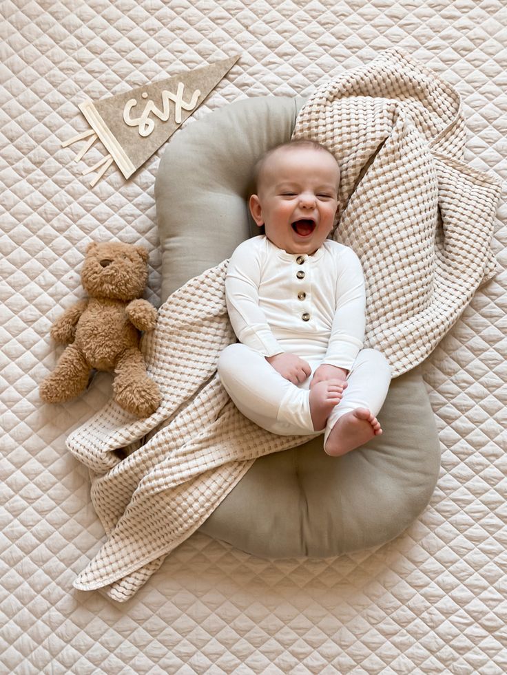 a baby laying on top of a pillow next to a teddy bear