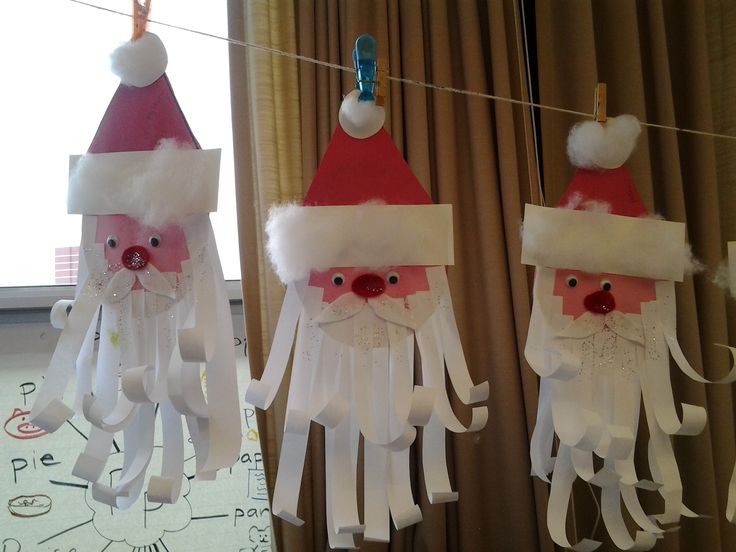 three paper santa clauss hanging from clothesline in front of window with drapes