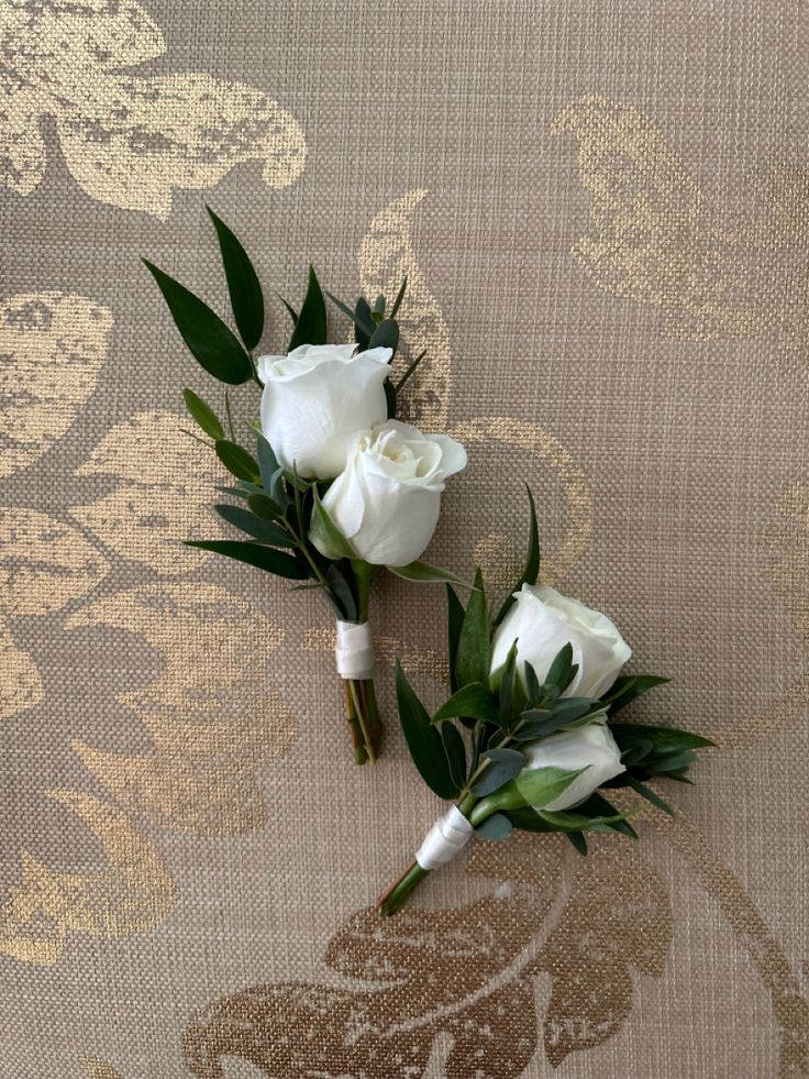 two white roses and greenery on a tan background