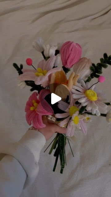 a person holding a bouquet of flowers on top of a white bed sheet in front of a window