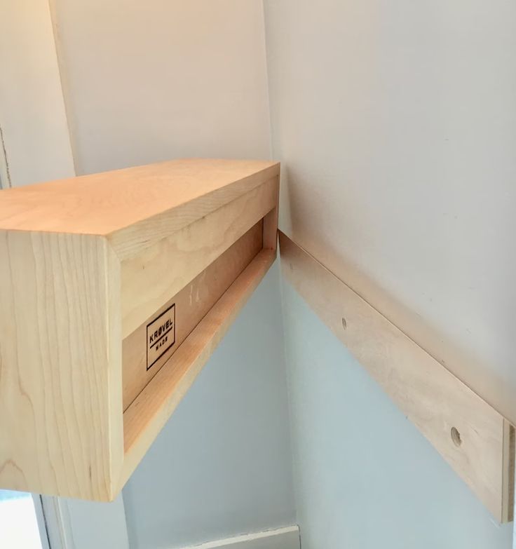 the corner of a room with a wooden shelf on one side and a closed drawer on the other