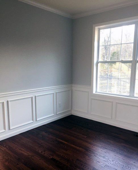 empty room with hard wood floors and white paneling on the walls, windows in the corner