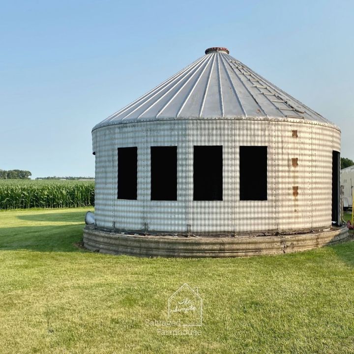 an old round building sitting in the middle of a field with windows on it's side