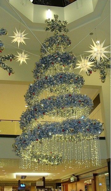 a christmas tree is hanging from the ceiling in a shopping mall, decorated with lights and snowflakes