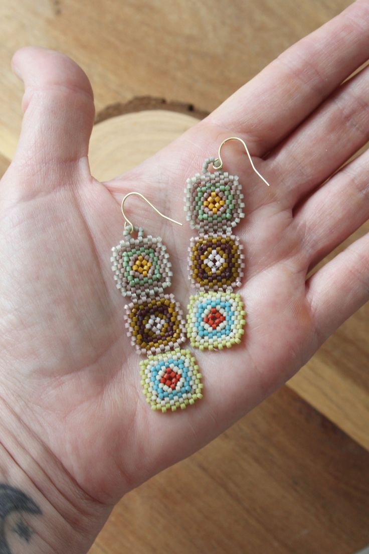 a hand holding three beaded earrings on it's left side, and the other two