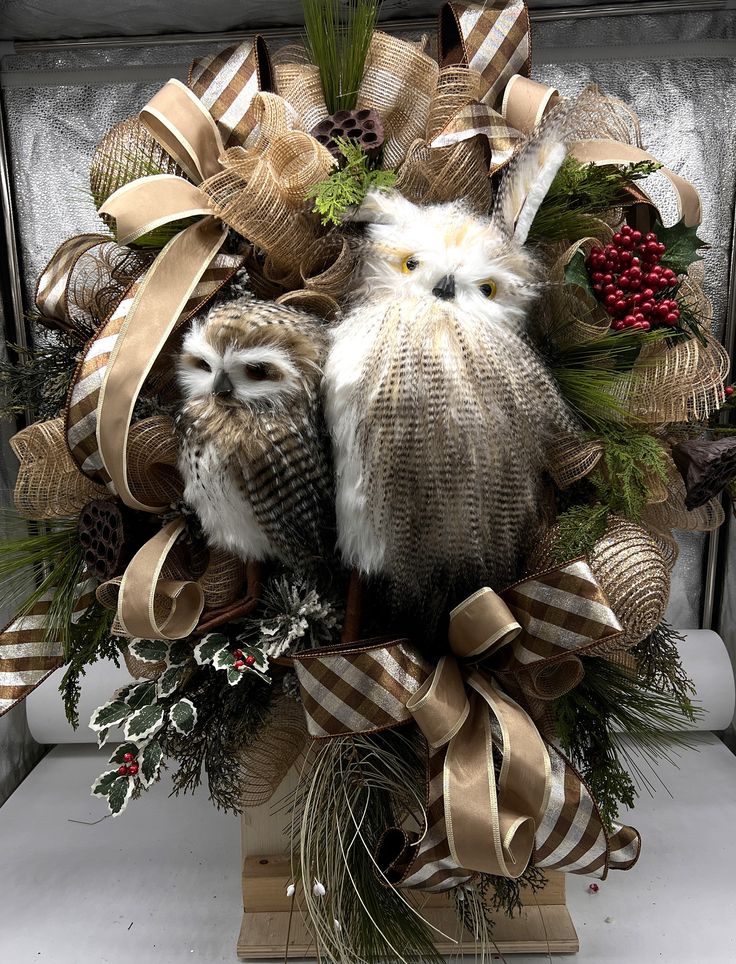 two owls are sitting on top of a christmas wreath with ribbons and pine cones around them