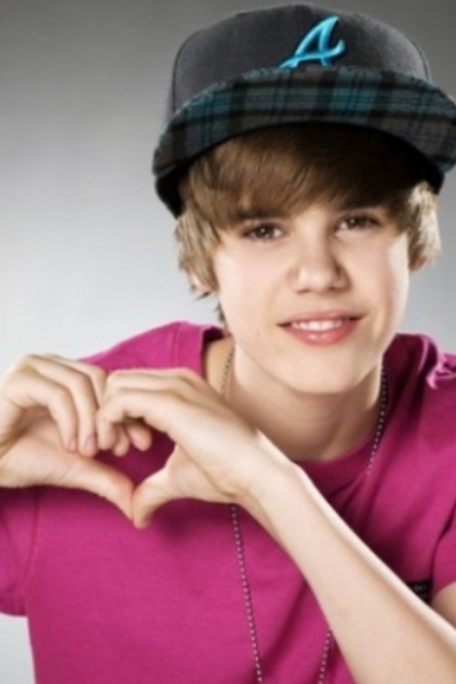 a young man in a pink shirt and cap making a heart shape with his hands