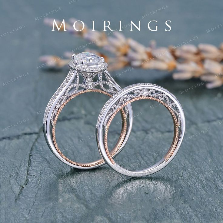 two wedding rings sitting next to each other on top of a stone surface with flowers in the background