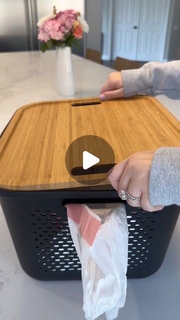 a person holding a plastic bag in front of a wooden cutting board on top of a table