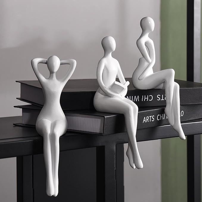 three white mannequins sitting on top of a book shelf next to each other