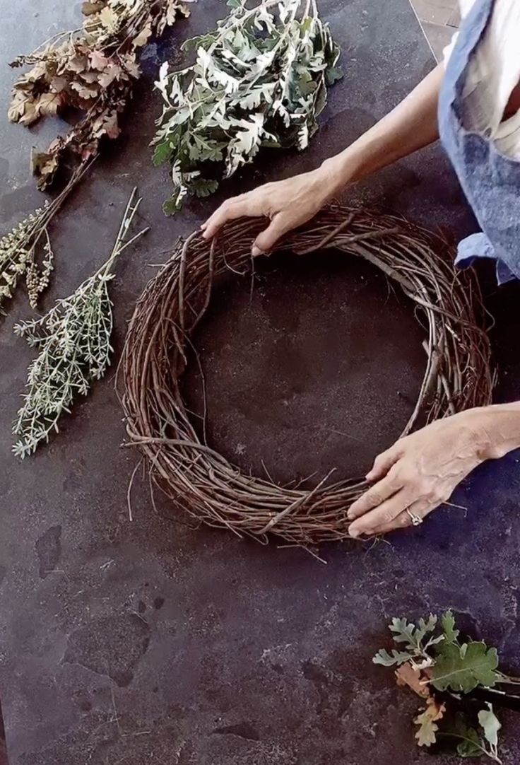 a woman is making a wreath out of twigs and dried herbs on a table top