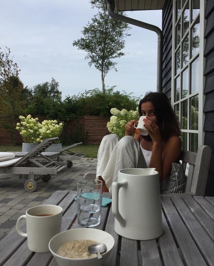 a woman sitting at a table drinking from a coffee cup next to two mugs