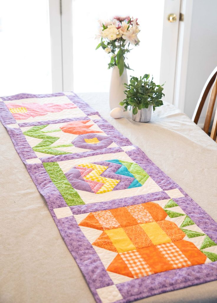 the table runner is made with quilts and has flowers in vase next to it