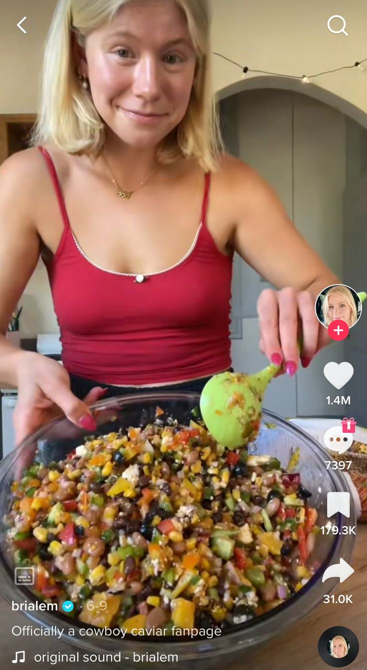 a woman in a red tank top is preparing a large bowl of food on the table