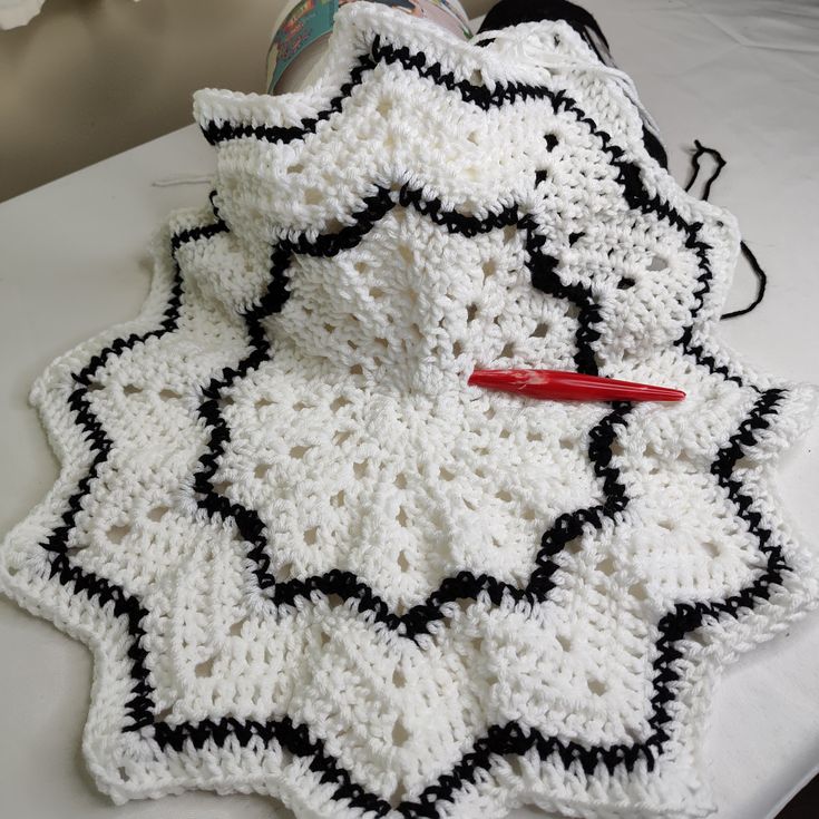 a crocheted white and black blanket with a red pen on the table next to it