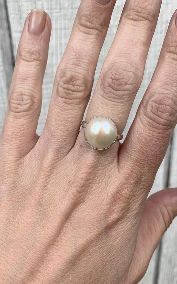 This elegant and stately pearl ring is made from a beautiful and unique white cream 14mm Mabe South Sea AAA Pearl that has many hues including pink. The pearl has been set in sterling silver with a sterling silver ring band handmade from half dome wire. This ring has some height, the setting is almost 1/2 inch high. The white cream pearl is more matte than the other mabe pearls listed, but still has a luminescent quality that makes it captivating!Made to order! Choose your size and your color pe Elegant Mother Of Pearl Round Rings, Elegant Oval Mother Of Pearl Ring, Cream Pearl Drop Jewelry For Anniversary, Wedding Pearl Ring In Mother Of Pearl, Wedding Pearl Ring With Mother Of Pearl, White Mother Of Pearl Wedding Ring, Elegant Round Mother Of Pearl Ring, Classic Mother Of Pearl Ring As Gift, Classic Mother Of Pearl Ring As A Gift