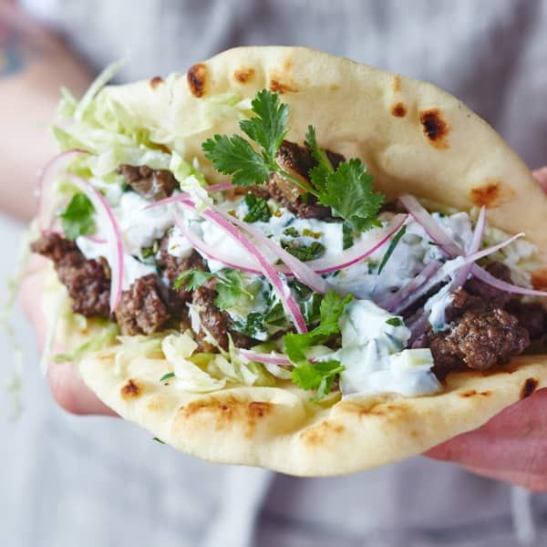 a person holding a taco filled with meat, onions and cilantro sauce