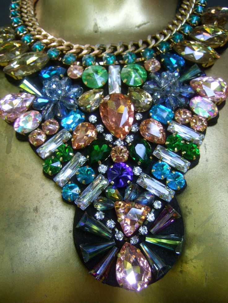 "Massive glittering crystal bib collar necklace The incredible huge scale bib style necklace is embellished with a collection of prong set glass crystals in a myriad of colors & shapes The top section of the necklace is designed with a rigid gilt metal chain framed with a wreath of emerald green color prong set crystals The lower section of the bib collar necklace is adorned with brilliant shimmering prong set crystals in a spectrum of colors that range from pink, pale & emerald green, a Glamorous Party Crystal Necklaces With Jewels, Glamorous Party Crystal Necklaces, Glamorous Jeweled Crystal Necklaces, Multicolor Rhinestone Necklace With Sparkling Stones For Party, Multicolor Crystal Necklace With Rhinestones, Rhinestone Jeweled Choker Necklace, Rhinestone Jewel Choker Necklace, Costume Jewelry Necklaces With Sparkling Stones, Multicolor Crystal Rhinestone Necklace With Sparkling Stones