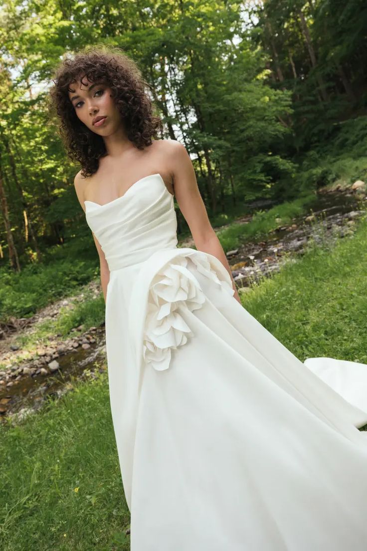 a woman in a white wedding dress standing on the grass with her hand on her hip