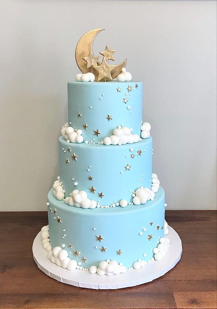 a three tiered blue cake with stars and moon on top, sitting on a wooden table