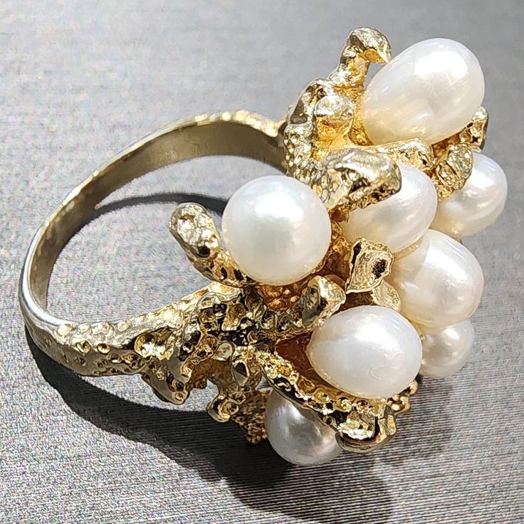 Experience the luxurious beauty of the our Estate 14K yellow gold Pearl ring, adorned with nine organic oval-shaped pearls with a rare coral-inspired texture. Finger size 6 in 14K yellow gold available for same day shipping. This ring can be sized up or down one size at no additional cost to you. Resizing takes 2 -3 business days. Includes ring box Includes jewelry appraisal Ships fully insured to point of delivery Free shipping on this item Estate Ring, Gold Pearl Ring, Estate Rings, Jewelry Appraisal, Textured Ring, Womens Wedding Bands, Shop Engagement Rings, Yellow Gold Ring, Gold Pearl