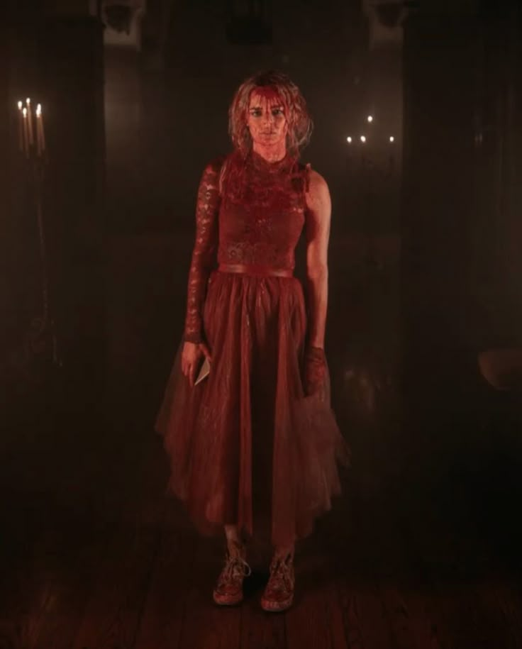 a woman in a red dress standing in the dark with her hands on her hips