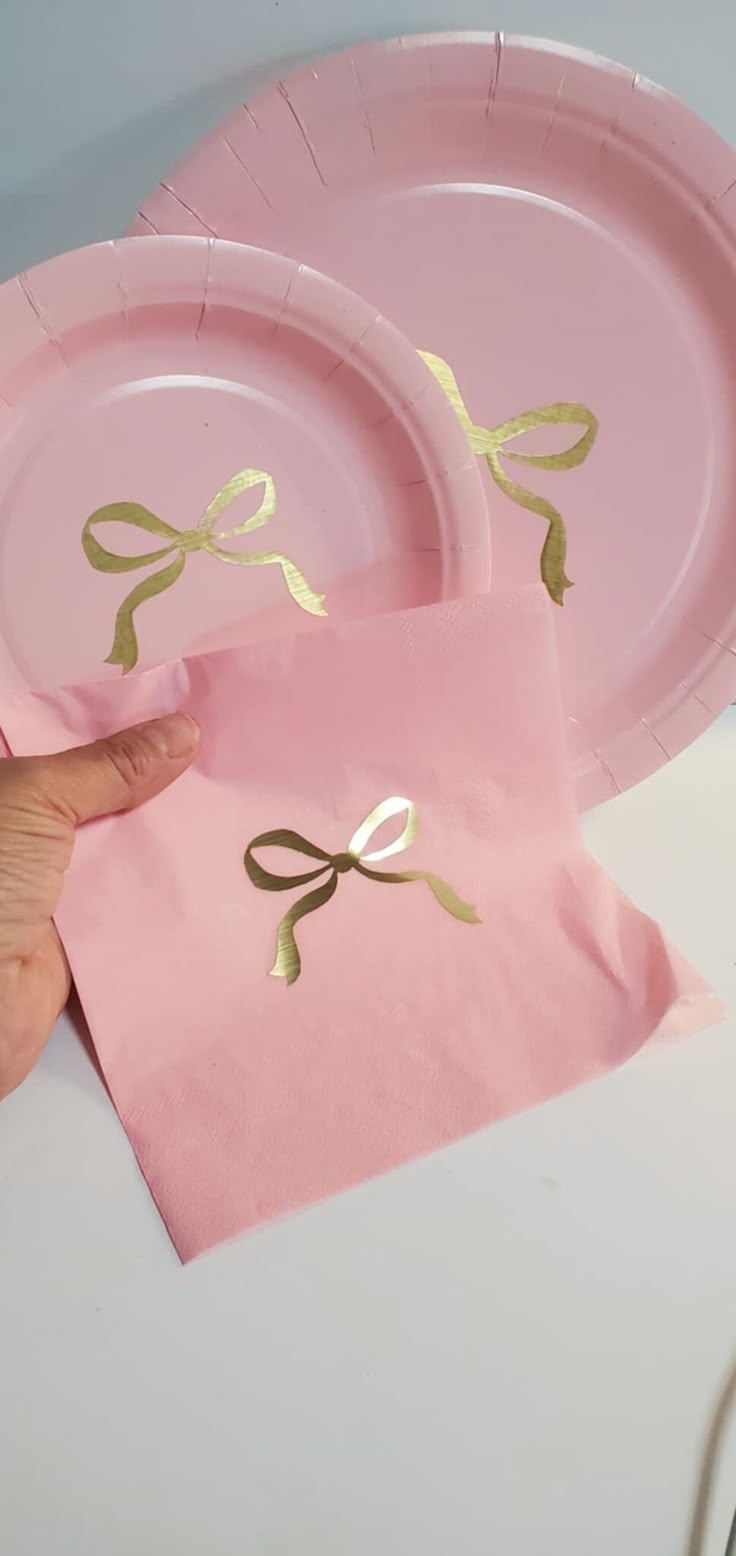 a pink paper plate with gold foil bows on it and napkins next to it