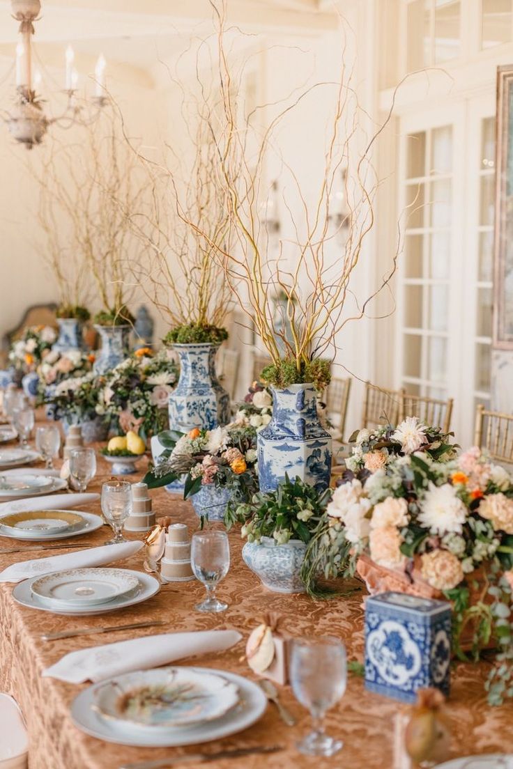 a long table is set with blue and white vases filled with flowers, plates and glasses