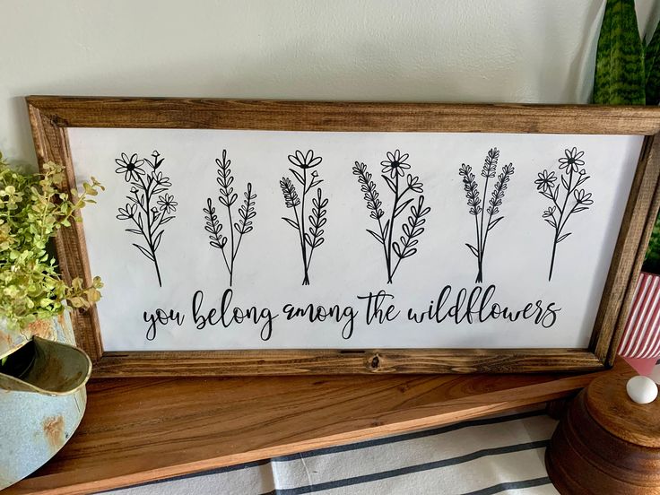 a sign that says, you belong among the wildflowers on a shelf next to a potted plant