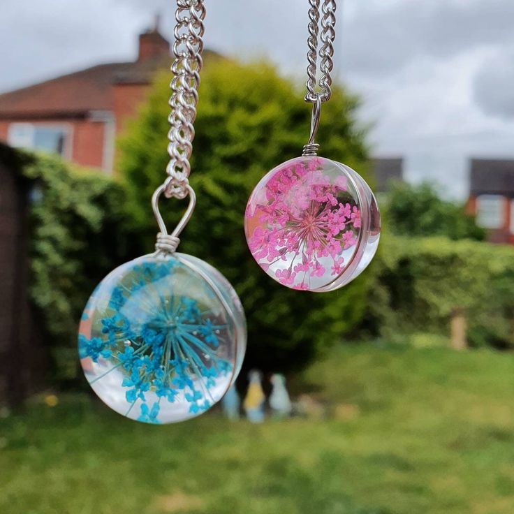 two glass pendants hanging from chains on a chain in front of some grass and trees