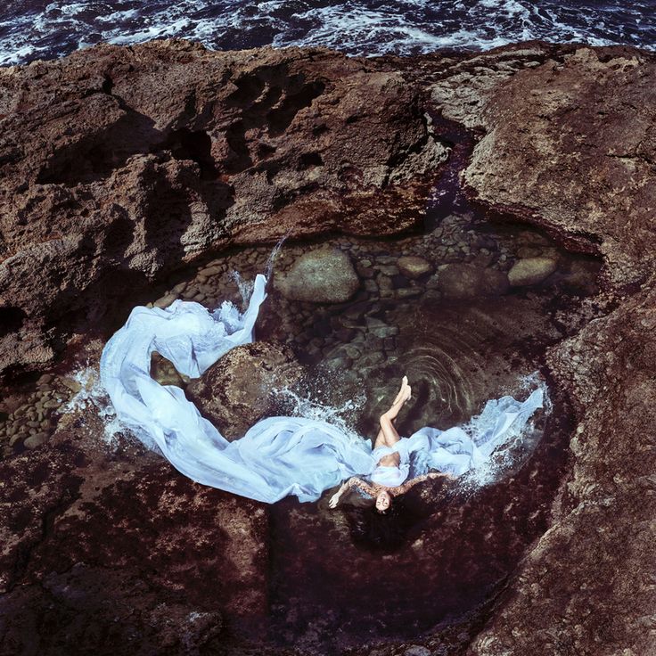 a woman laying on top of a rocky beach next to the ocean in a white dress