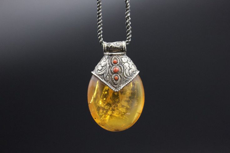 A very unique Hand made Silver Pendant with a replica Amber. Amber is used by Tibetans for centuries. High-quality amber is rare and expensive. The replica is commonly used with Silver as jewelry. In this piece, amber is decorated beautifully with carved silver that has an Auspicious symbol conch shell, flora pattern and coral cabs. Wt: 26g Origin- Nepal 20th c Bohemian Carved Amber Jewelry, Antique Engraved Amber Jewelry, Traditional Amber Jewelry With Carved Details, Vintage Carved Amber Jewelry, Handmade Antique Amber Jewelry, Vintage Amber Carved Jewelry, Collectible Bohemian Amber Jewelry, Handmade Amber Necklace For Collectors, Handmade Baltic Amber Spiritual Jewelry