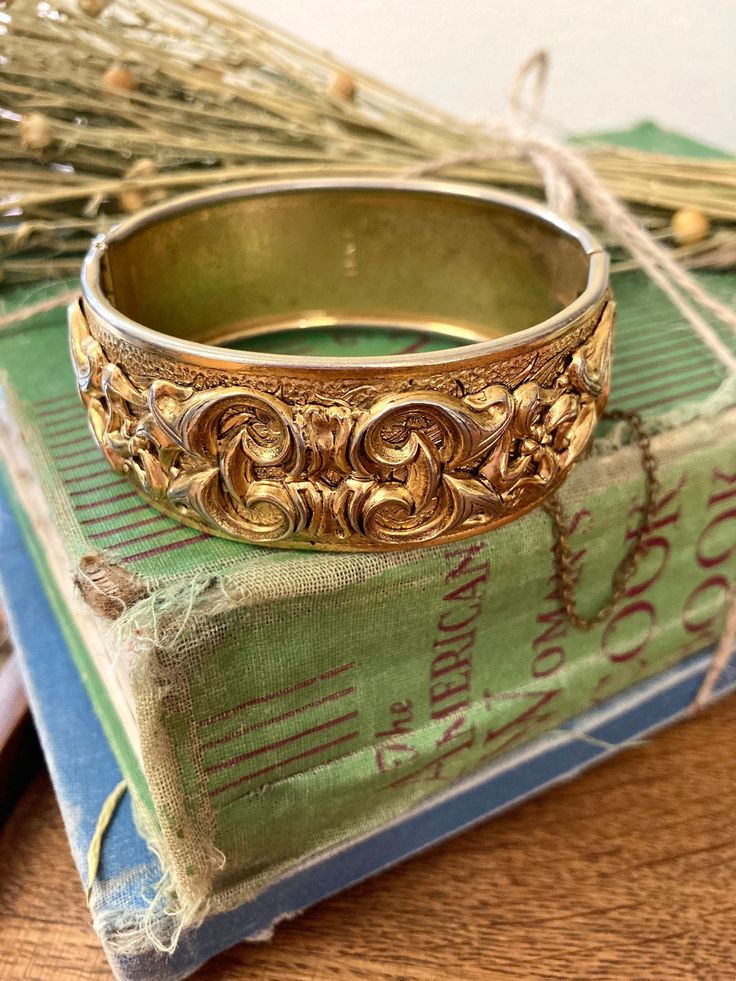 Goldtone  designer signed Lisner, unique classic art nouveau style design bangle bracelet.  Note this is a much older Lisner piece.  It features a  wonderful scrolled etched raised relief floral and leaf eternity style design. This is an amazing bracelet, having all of the highly sought after qualities of the ever popular art nouveau style era of jewelry. It is bold measuring app. 3/4 inches wide . Its exterior diameter is 2.5 inches. Hinged with safety chain. Stamped Lisner on the inside. Has one black spot on the exterior. Overall great condition. Elegant Antique Finish Bangle Bracelet, Elegant Bangle With Antique Finish, Elegant Bangle Bracelet With Antique Finish, Victorian Etched Cuff Bracelet, Victorian Etched Cuff Bracelet For Wedding, Antique Cuff Bracelet With Intricate Design For Formal Occasions, Antique Etched Bangle For Wedding, Victorian Engraved Cuff Bracelet For Anniversary, Vintage Engraved Bracelets For Wedding