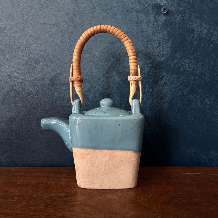 a ceramic teapot with a handle on a wooden table next to a blue wall