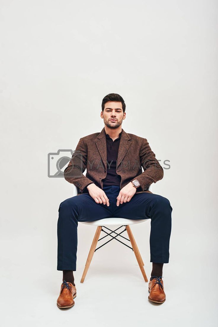 a man sitting on top of a chair with his hands in his pockets and legs crossed